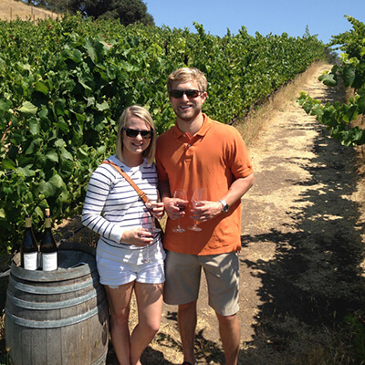 Couple with glasses of wine standing in vineyard