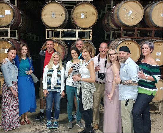 Wine tour group standing and smiling in front of wine casks