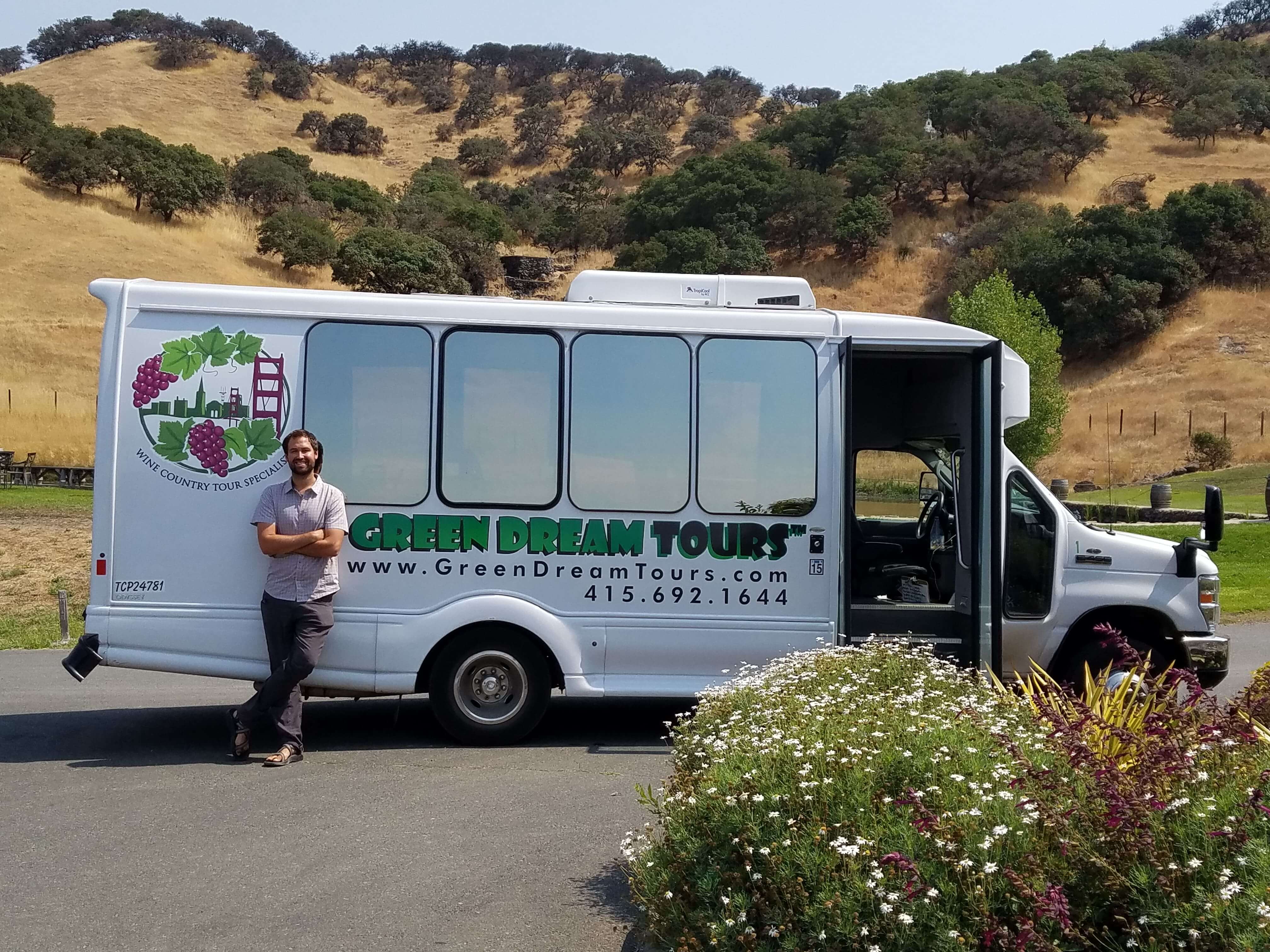 Man in front of white exterior of Green Dream Tour bus at vineyard
